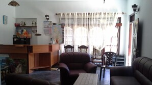 A living room with a sofa, armchair, and a small table. There is a wooden desk with a chair and a shelf with various items. - Prasad Suomi Villa (Matara)