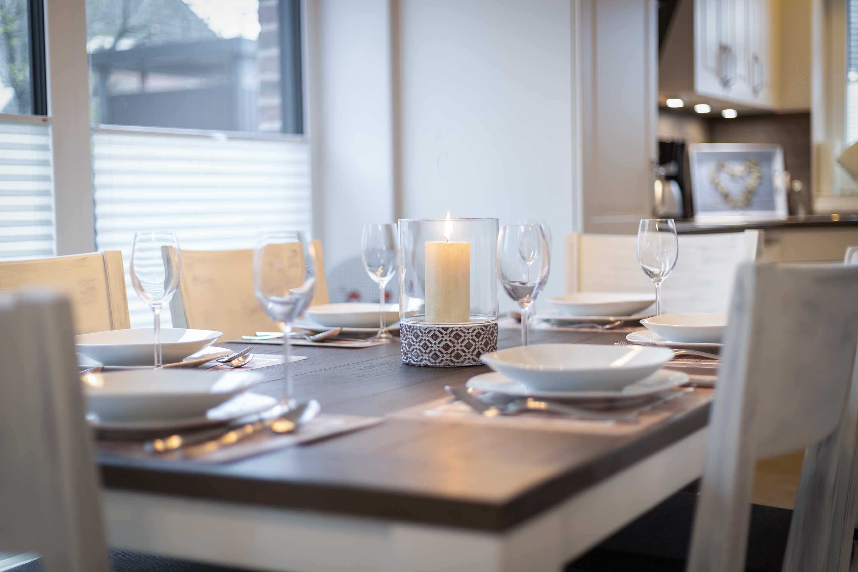 Een eettafel gedekt met borden, glazen en een kaars als decoratie.
