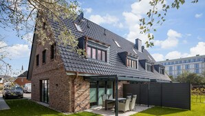 Ett modernt hus med en fasad av tegel, ett sluttande tak och en täckt uteplats med utemöbler.