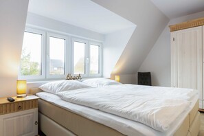 A bedroom with a large bed, two bedside lamps, a nightstand, a wardrobe, and a window with a view.