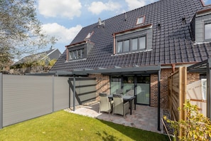 A modern house with a tiled roof, a covered patio with outdoor furniture, and a fenced backyard.