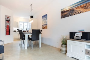A modern dining area with a white table and chairs, a pendant light, and artwork on the walls.