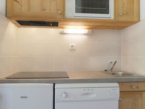 A kitchen with wooden cabinets, a microwave, a dishwasher, and a sink. - Cozy 2-Room Cabin, Southern Exposure, Ski-in/Ski-out, Pets Allowed (Méribel)