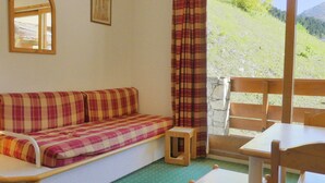 A cozy room with a sofa, a small table, and a chair. There's a window with curtains, a mirror, and a framed picture on the wall. - Cozy 2-Room Cabin, Southern Exposure, Ski-in/Ski-out, Pets Allowed (Méribel)