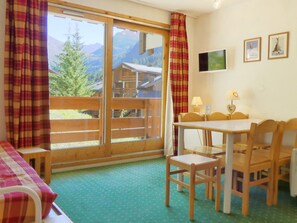 Une pièce avec une table en bois, des chaises, un lit avec des rideaux à carreaux, une télévision et une vue sur la montagne.