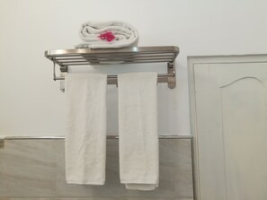A bathroom with a towel rack holding two white towels and a folded towel with a pink flower. - Flamingo Nature Resort (Weerawila)