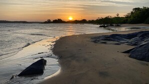 Une plage où l’on peut admirer le coucher de soleil, avec une eau calme et un rivage sablonneux parsemé de rochers.