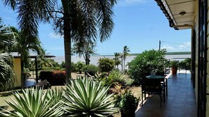 Une terrasse offrant une vue sur un plan d’eau, entourée de différentes plantes et agrémentée d’une table et de chaises.