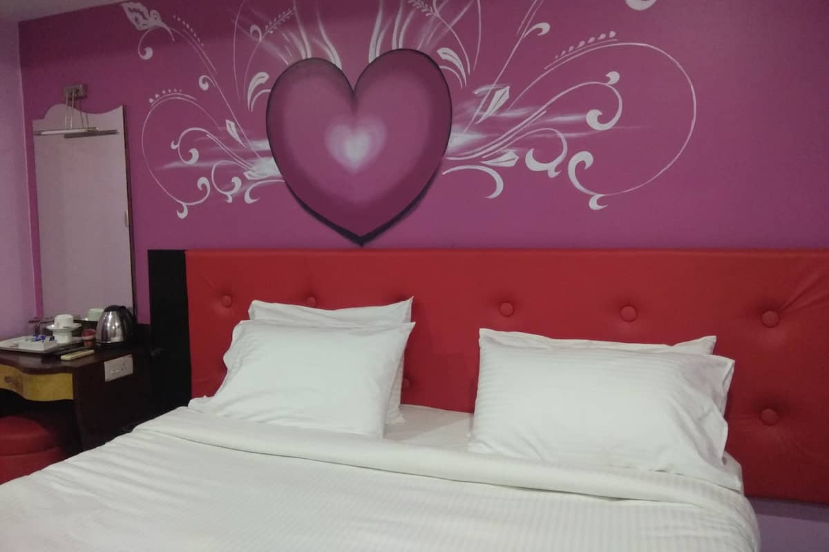A room with a red headboard, white bedding, and a wall with a decorative heart and floral patterns.