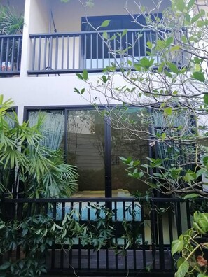 A modern two-story building with balconies, large windows, and lush greenery.