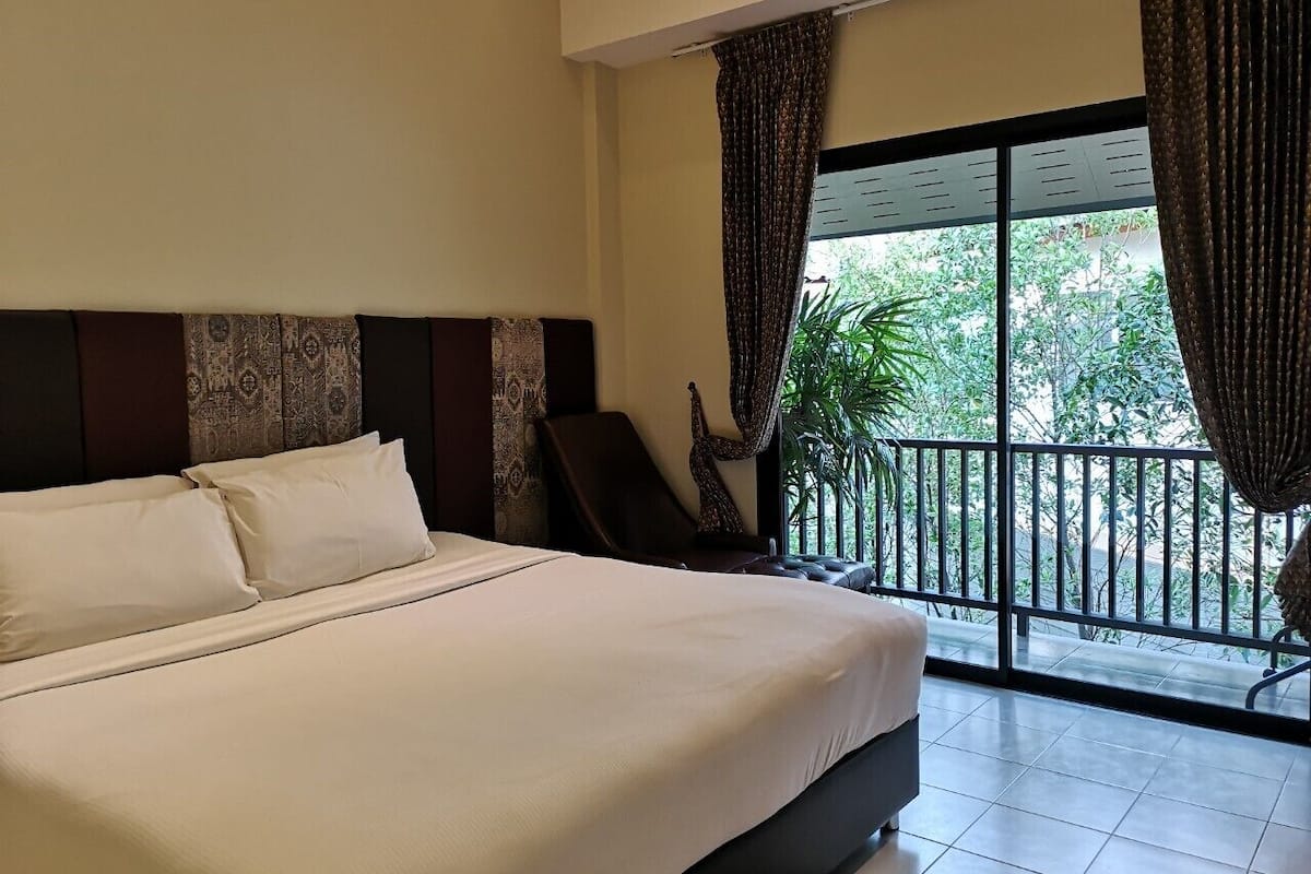 Hotelkamer met een groot bed, een stoel, een raam met gordijnen en uitzicht op groen.