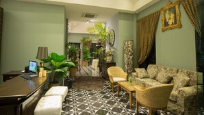 Een hotellobby met een receptiebalie, een zithoek en decoratieve planten.