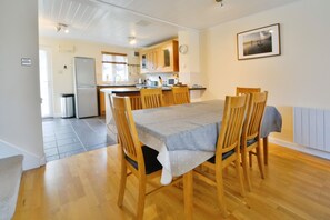 A dining area with a wooden table and chairs, a kitchen in the background, and a framed picture on the wall.