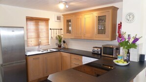 A modern kitchen with wooden cabinets, a stainless steel refrigerator, a built-in microwave, and a sink.