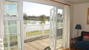 A room with a wooden deck, a view of a lake, a white railing, and a blue sofa.