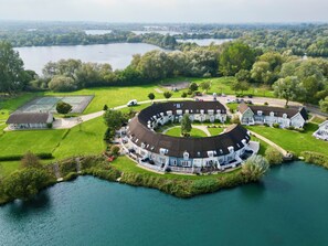 Un ensemble de bâtiments de forme circulaire comprenant un court de tennis, entouré d’un lac et de verdure.