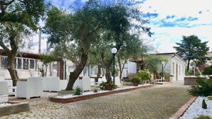 Un patio con mesas al aire libre, plantas en macetas y un camino adoquinado.