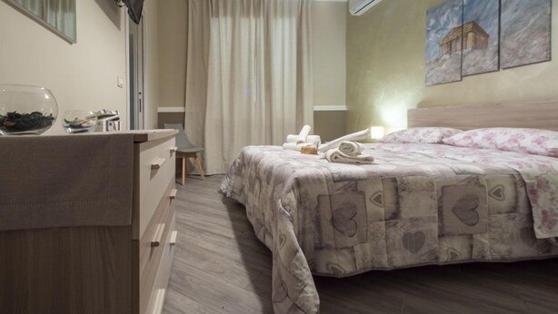 Un dormitorio con una cama, una mesita de noche, un espejo y una ventana con cortinas.