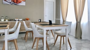 Un comedor con sillas y mesas blancas, una estación de café y un cuadro de comida en la pared.