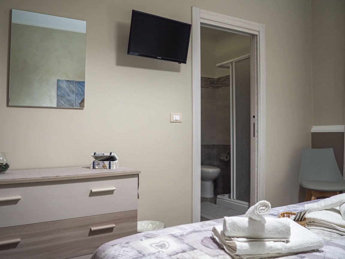 A hotel room with a bed, a bedside table, a TV mounted on the wall, and a bathroom with a shower and toilet.