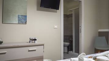 A hotel room with a bed, a bedside table, a TV mounted on the wall, and a bathroom with a shower and toilet.