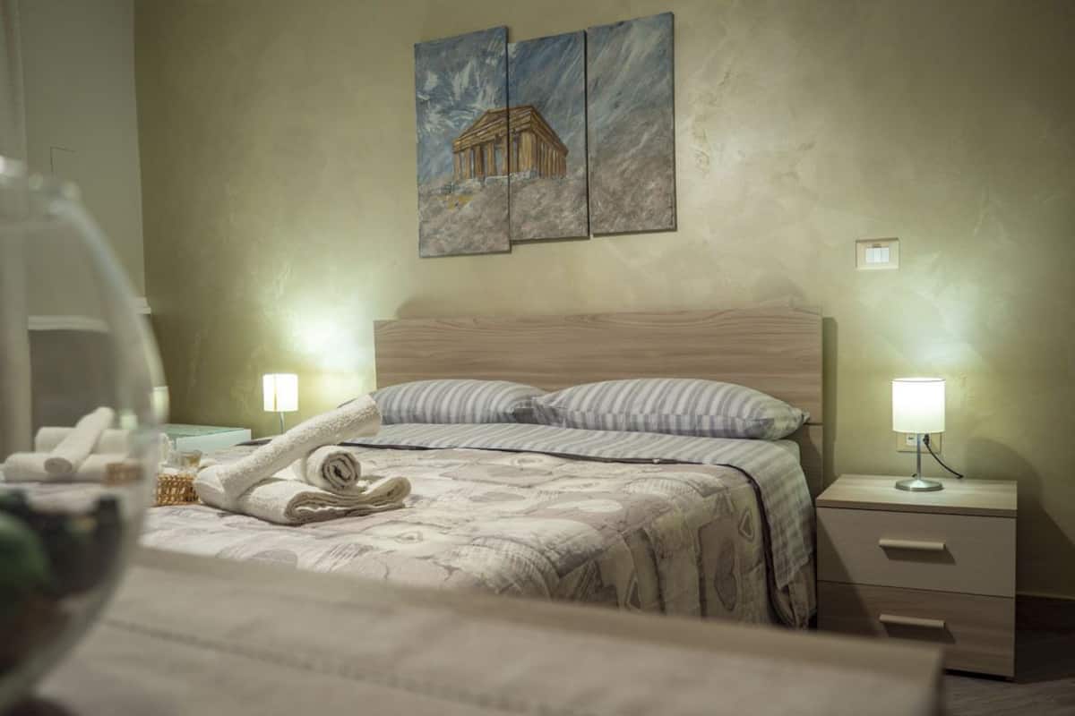 A hotel room with a bed, two bedside lamps, a nightstand, and a wall-mounted painting.