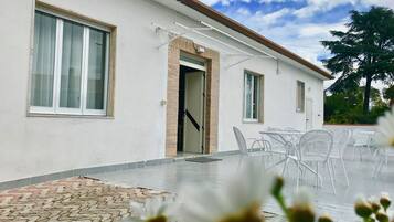 Ein modernes Gebäude mit großen Fenstern, einer Tür und einer Terrasse mit weißen Stühlen.
