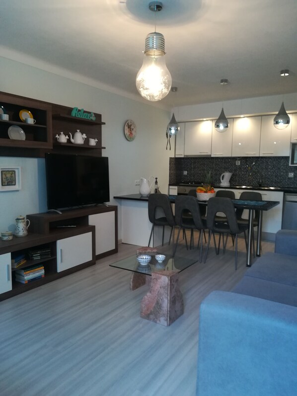A modern living room with a flat-screen TV, a glass coffee table, and a sofa. There is a kitchen area with a dining table and chairs. - CASA DA ROSEIRA - your holiday home with private garden (Famalicão)
