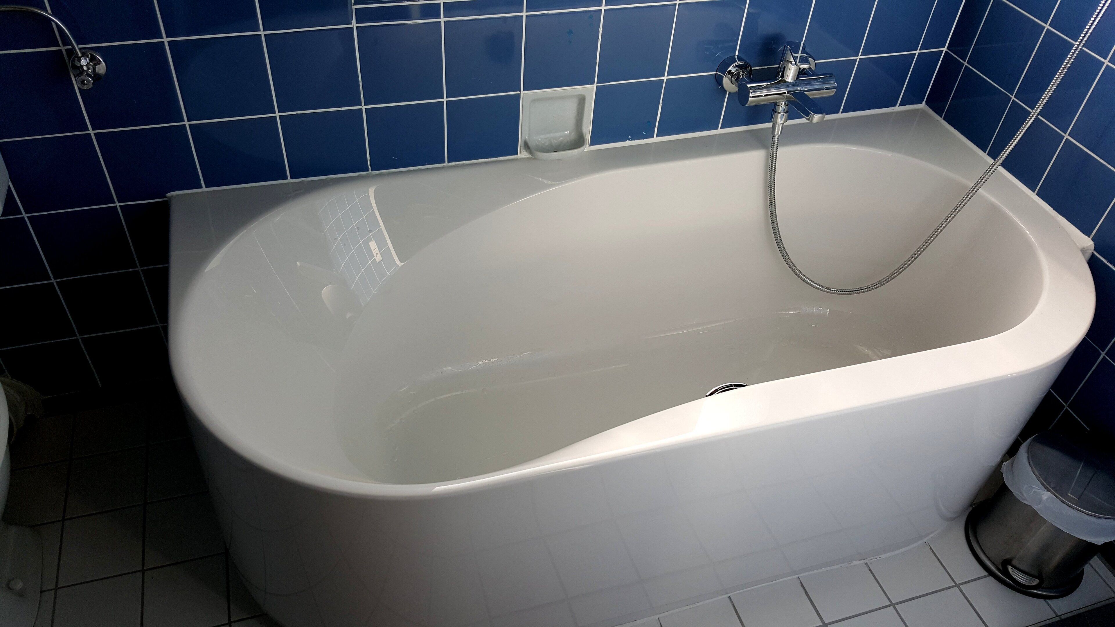 A white bathtub with a handheld showerhead in a bathroom with blue tiled walls.