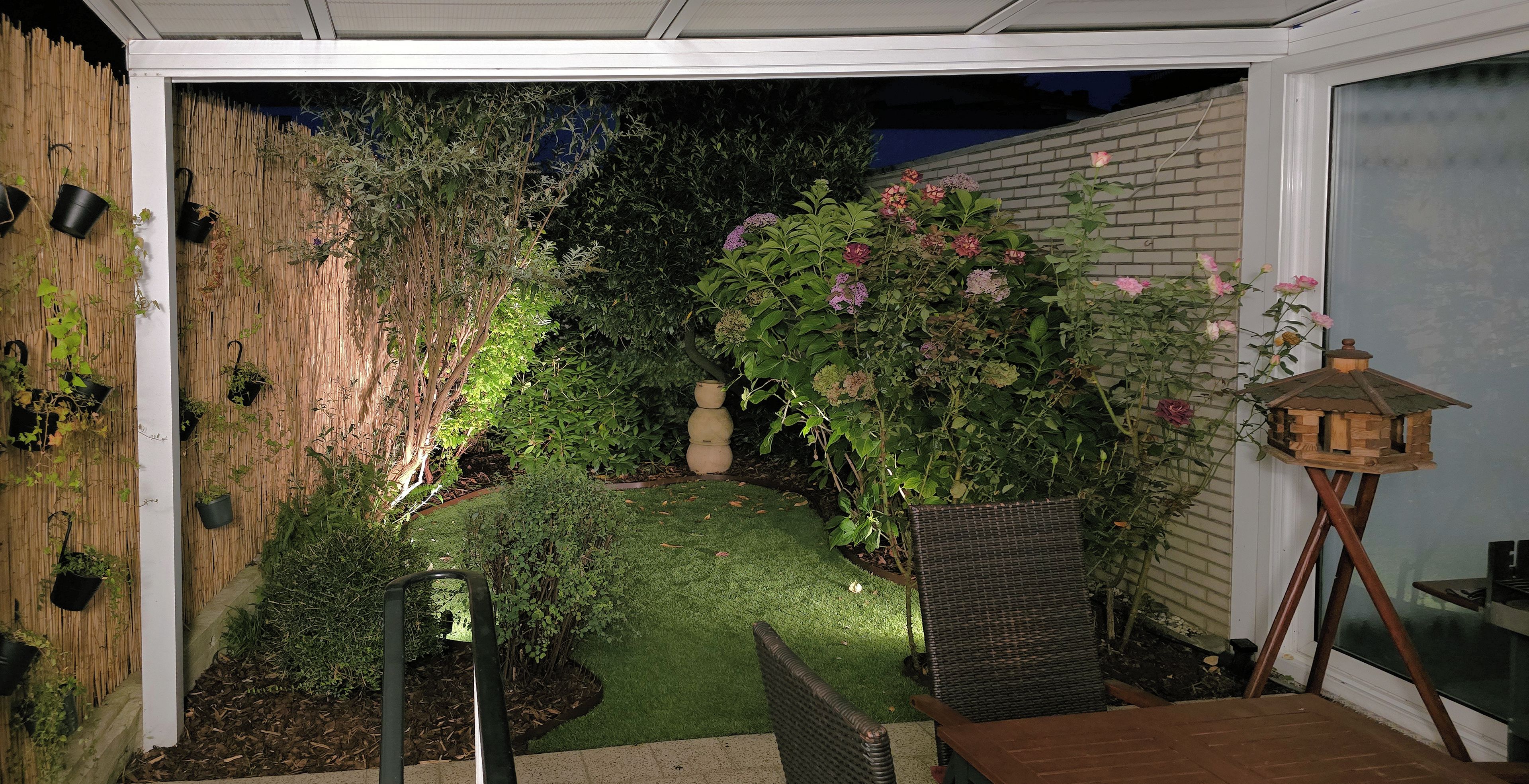 Ein Garten mit Holzzaun, Blumentöpfen, einem Vogelhäuschen und einem kleinen Tisch.