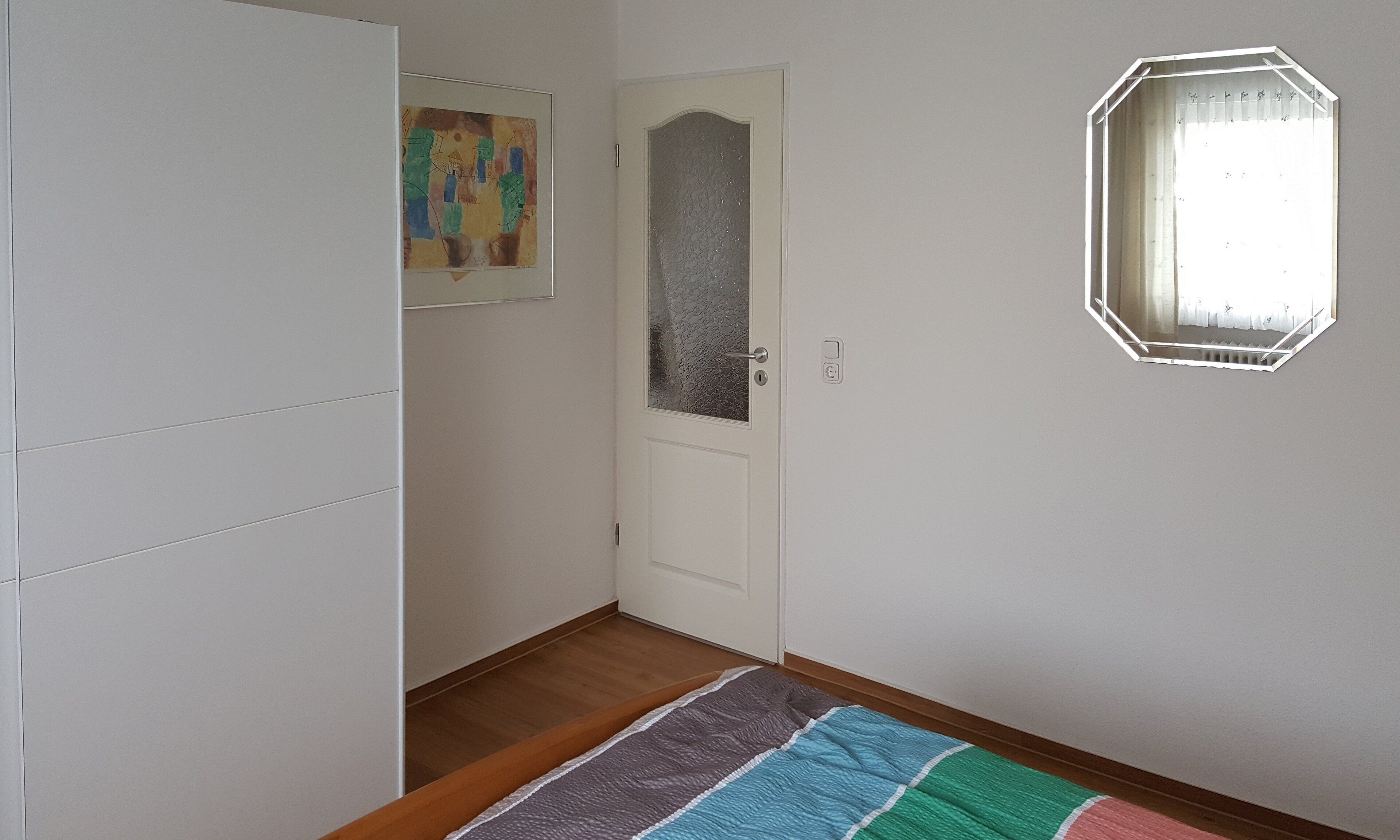 Ein Flur mit einer weißen Tür, einem gerahmten abstrakten Gemälde und einem Spiegel an der Wand.
