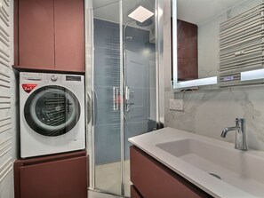 Um banheiro moderno com box de vidro, máquina de lavar embutida e pia com bancada de mármore.
