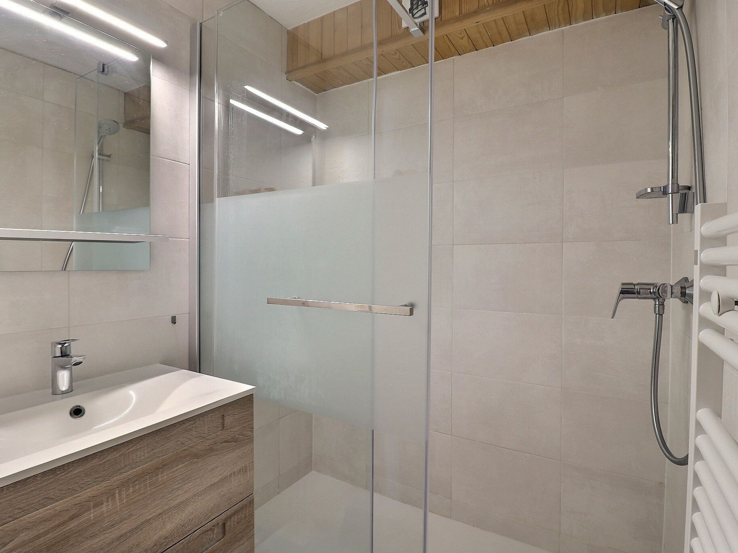 Un bagno moderno con cabina doccia in vetro, mobile bagno in legno e lavandino bianco.