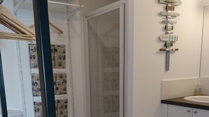 A modern bathroom with a shower, toilet, and sink. There is a towel rack with folded towels and a wooden door with a glass panel. - Emerald Coast Studio  (Saint-Méloir-des-Ondes)