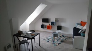 A modern loft apartment with a dining area, a sofa, and a TV mounted on the wall. - Emerald Coast Studio  (Saint-Méloir-des-Ondes)