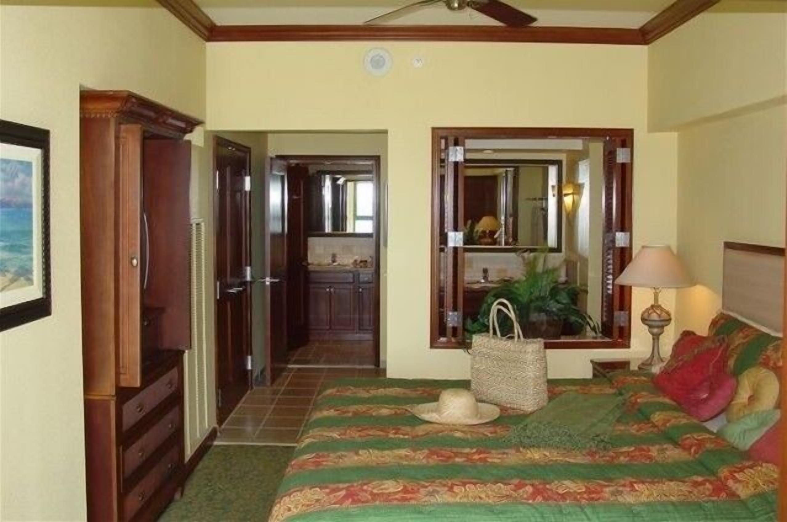 Une chambre d’hôtel avec un lit, un miroir, une commode, une lampe et une vue sur la cuisine.