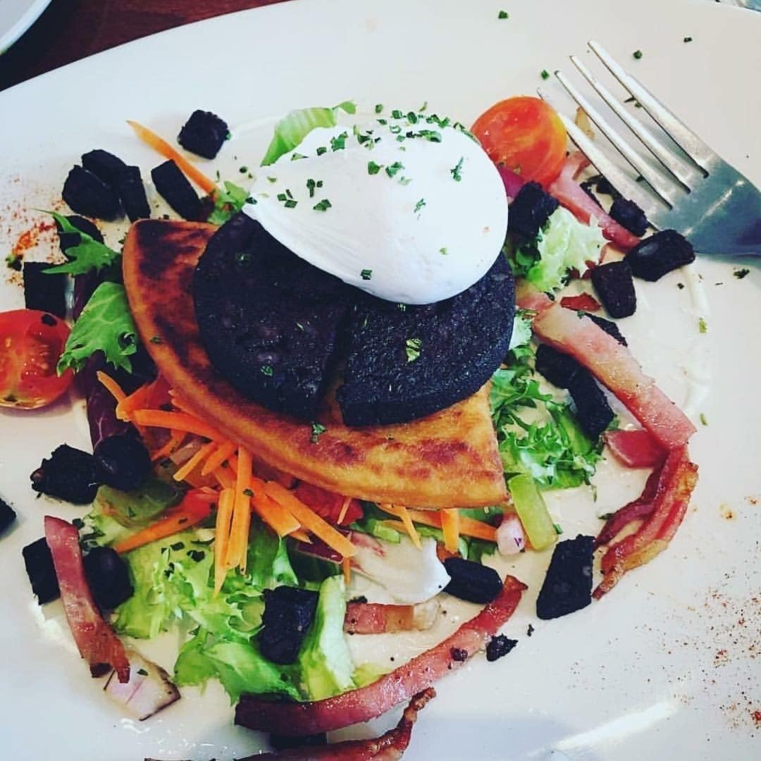 Un plato de comida con varios vegetales, un trozo de carne y una cucharada de salsa.