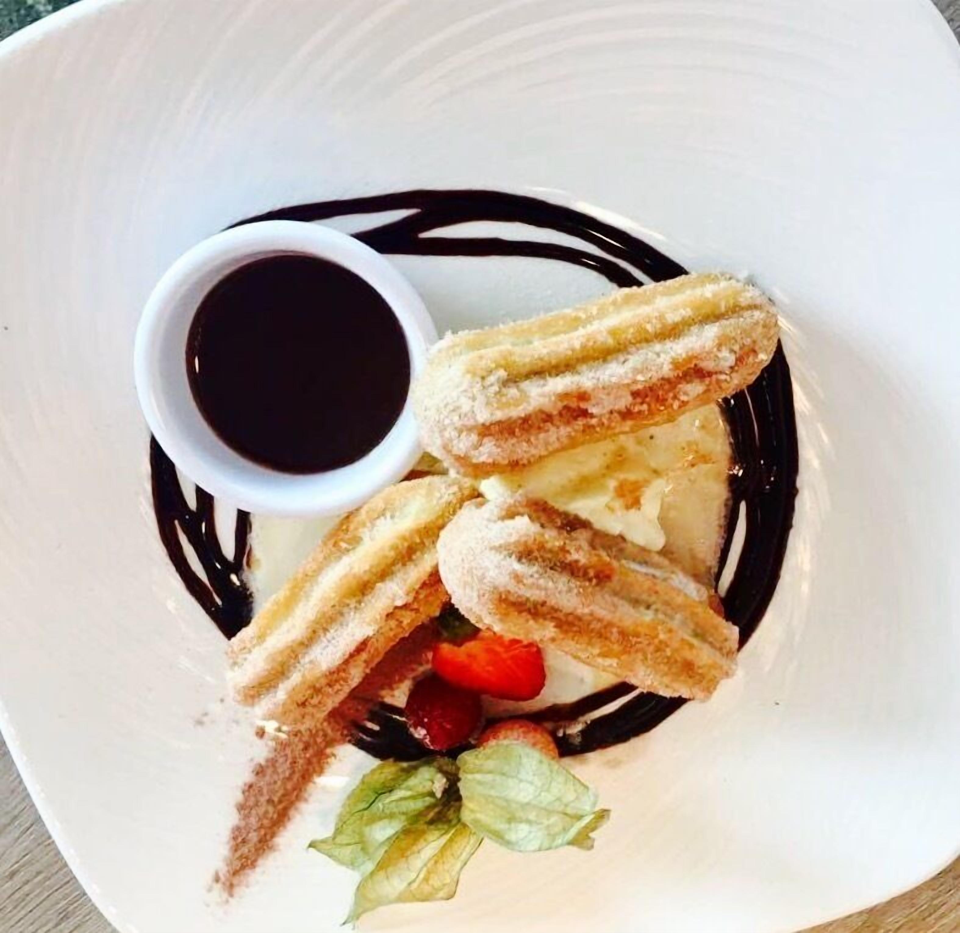 A plate with churros, a small cup of chocolate sauce, and a strawberry.