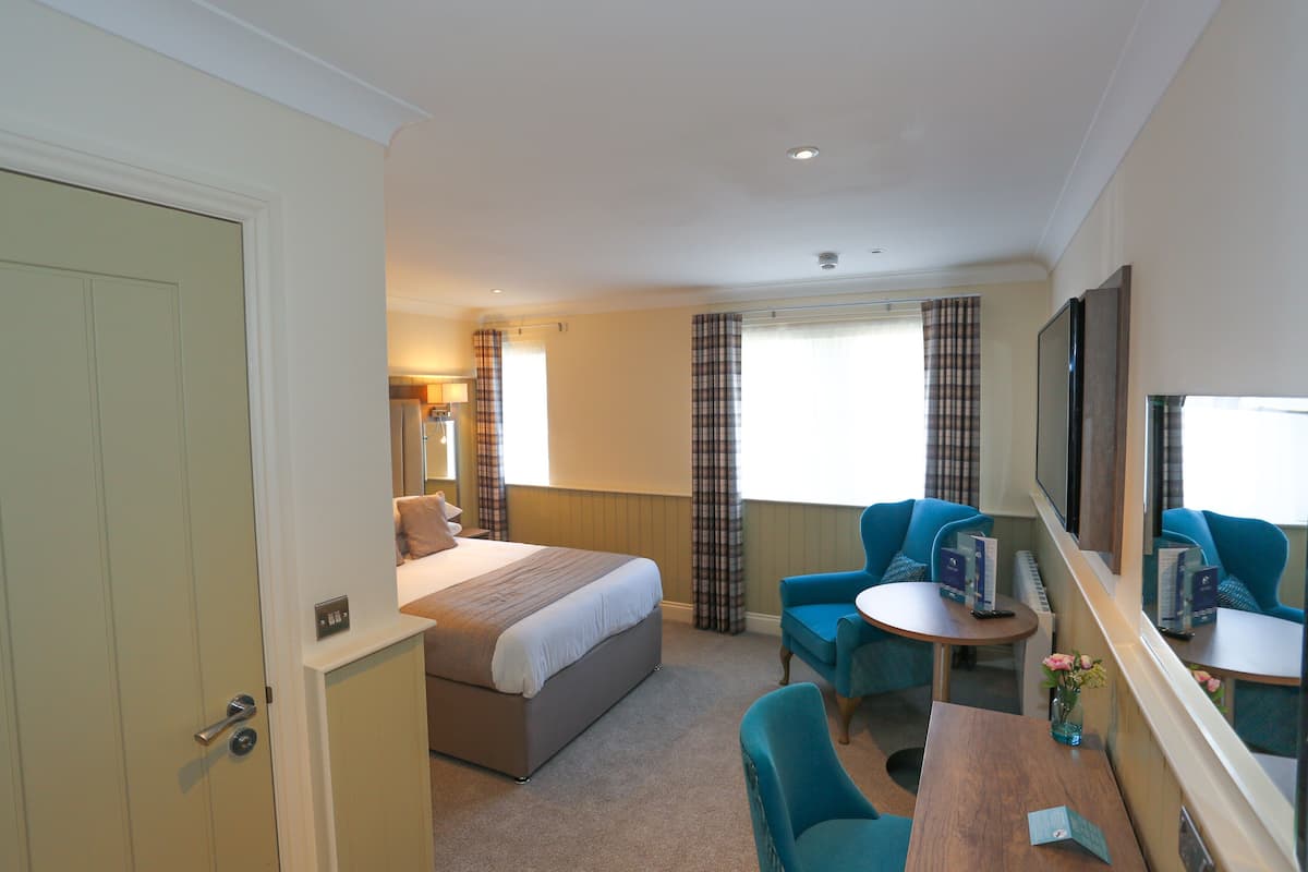 A hotel room with a bed, a desk, a chair, a TV, and a window with curtains.