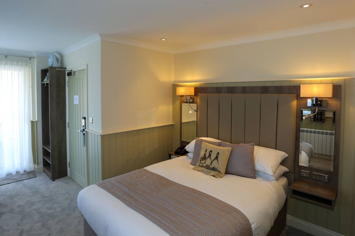 A hotel room with a large bed, bedside lamps, a wardrobe, and a mirror.