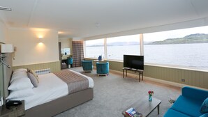 A bedroom with a bed, a TV, a coffee table, and a view of the water. - Duck Bay Hotel (Alexandria)