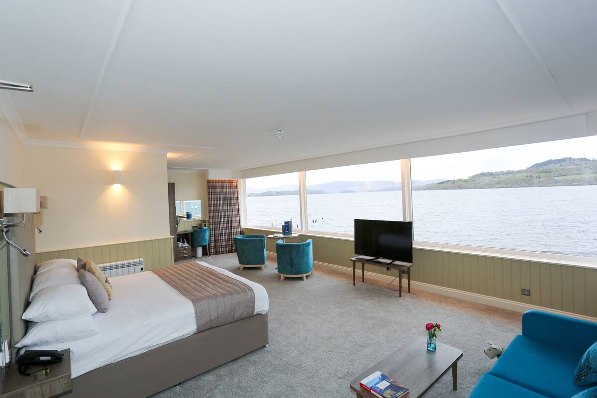 A bedroom with a bed, a TV, a coffee table, and a view of the water.