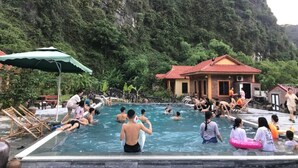 Une piscine où se baignent des gens, un bâtiment avec un toit rouge et, en arrière-plan, un paysage montagneux.
