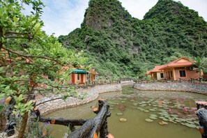A serene garden with a pond, stone bridge, and traditional buildings. - An Ngoc Tam Coc Bungalow (Nam Hoa Lu)