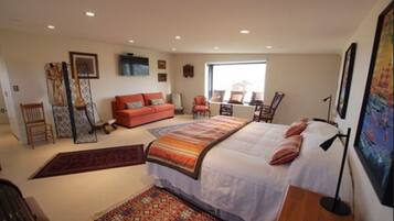 Un dormitorio con cama, sofá, sillón, escritorio y ventana.