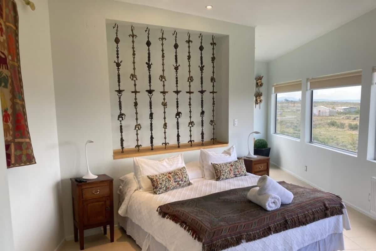 Une chambre à coucher avec un grand lit, une table de chevet, un élément décoratif fixé au mur et une fenêtre donnant sur un beau paysage.