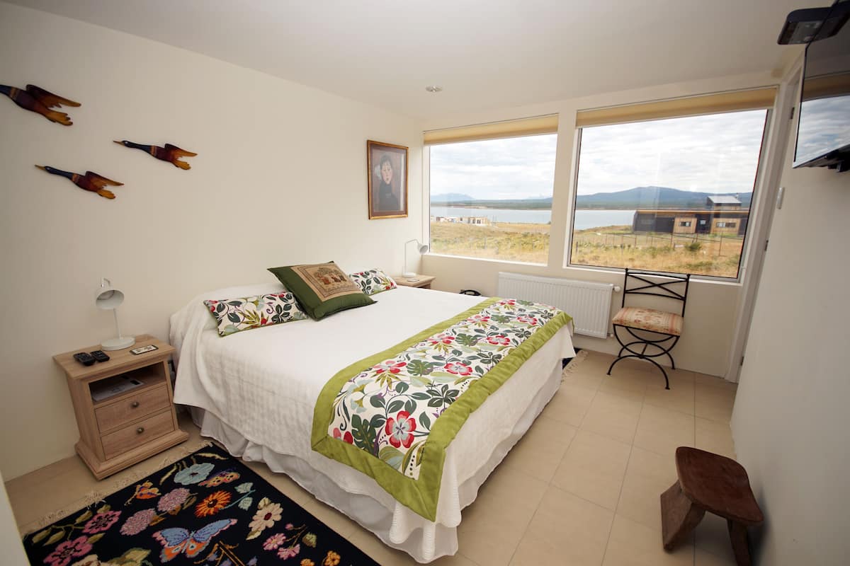 Une chambre à coucher comprenant un lit, une table de chevet, une chaise et donnant sur l’extérieur.