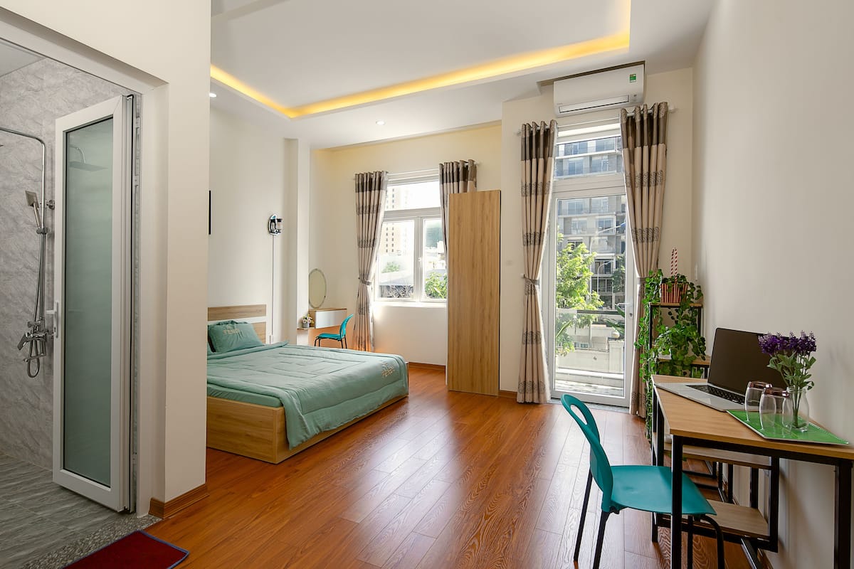 A modern bedroom with a bed, a desk with a laptop, and a shower area.