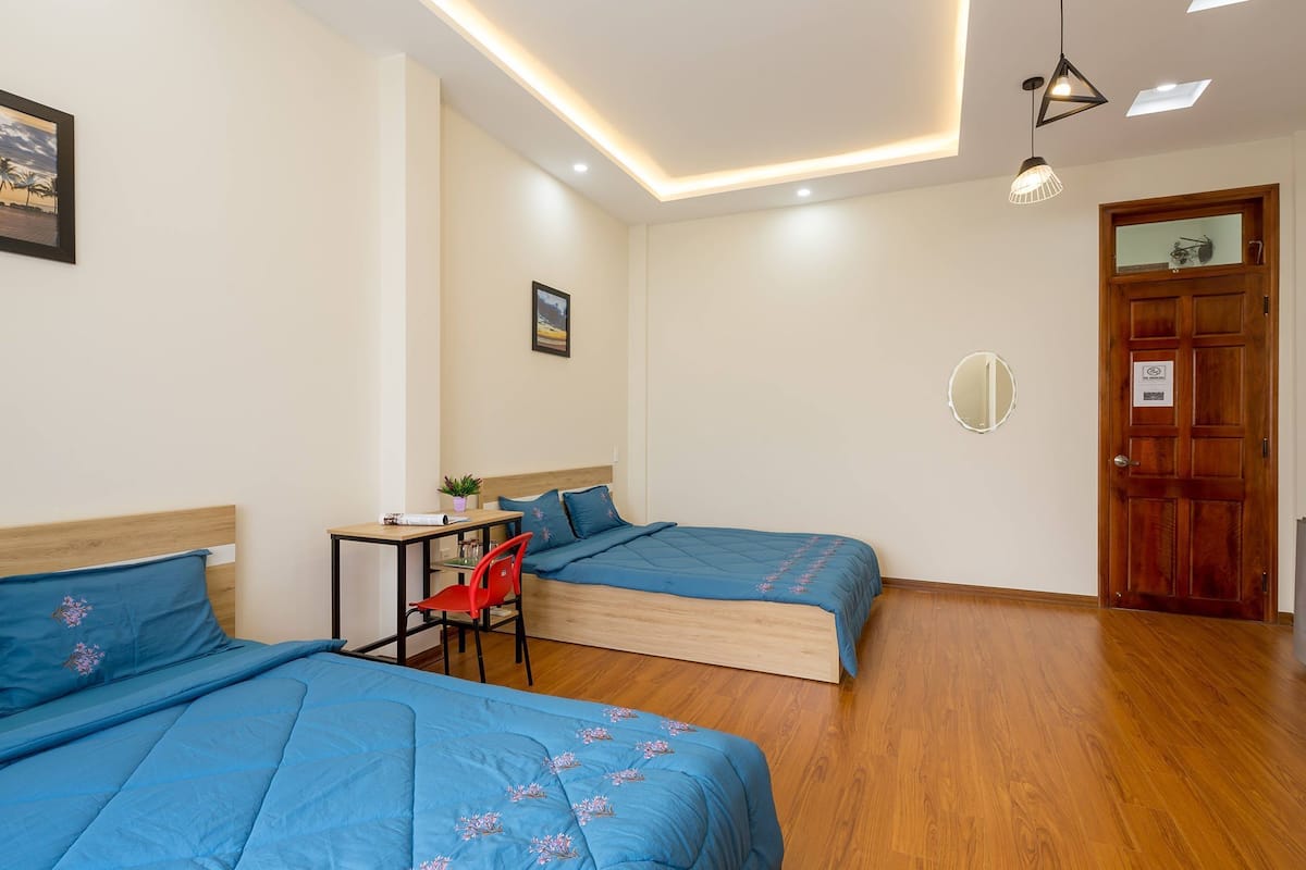A hotel room with two beds, a desk, a chair, a small table, and a door.