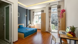 A modern bedroom with a bed, a desk with a laptop, a dining table with fruit, and a view of the city through large windows. - 10 Dollar Homestay Danang - Hostel (Da Nang)